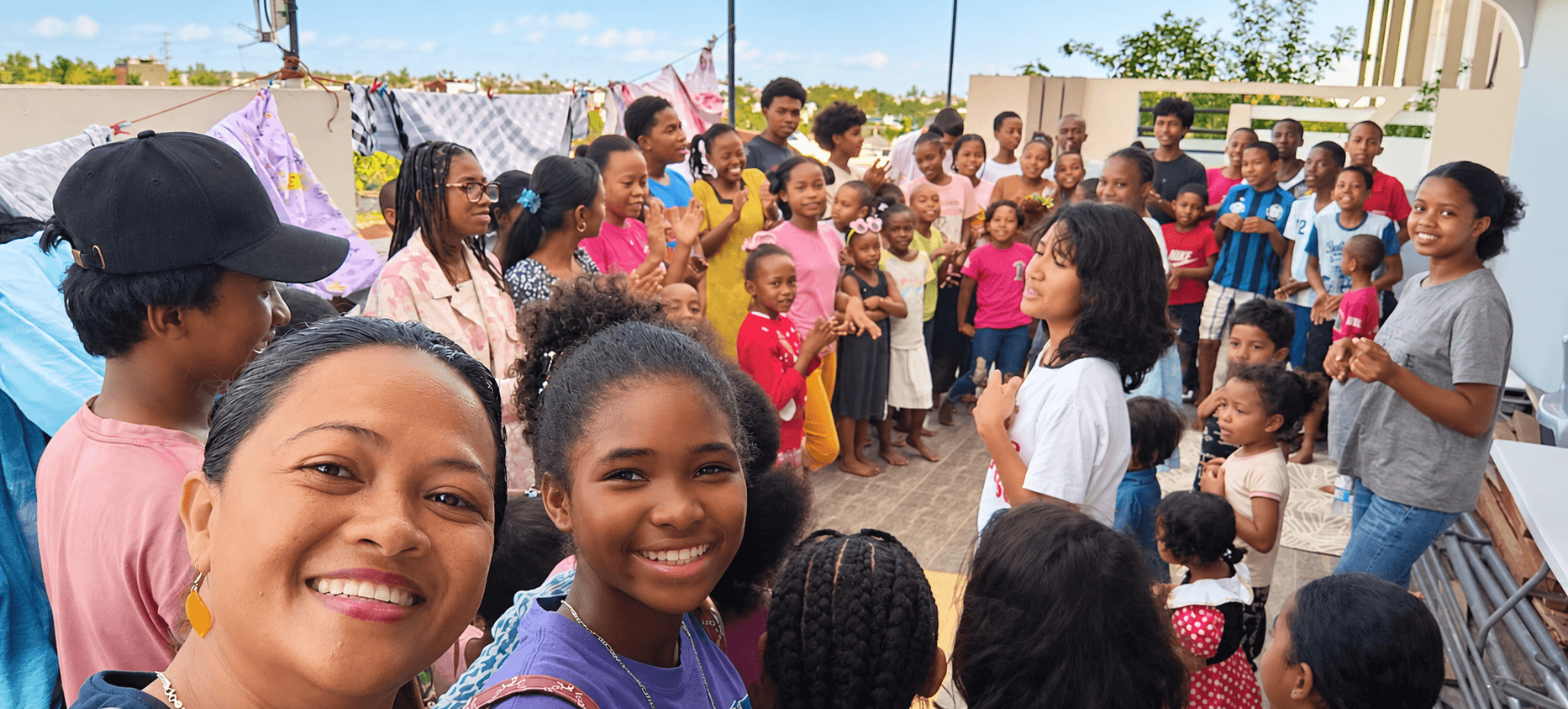 A smiling woman and girl in the foreground with children and adults gathered in Madagascar
